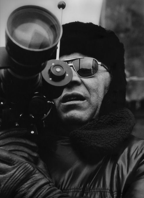 El director Sergio Corbucci con cámara de cine durante un rodaje, con gorro de invierno y gafas de sol