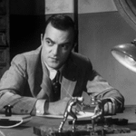 El actor italiano Franco Giacobini sentado en un escritorio, en una escena en blanco y negro

