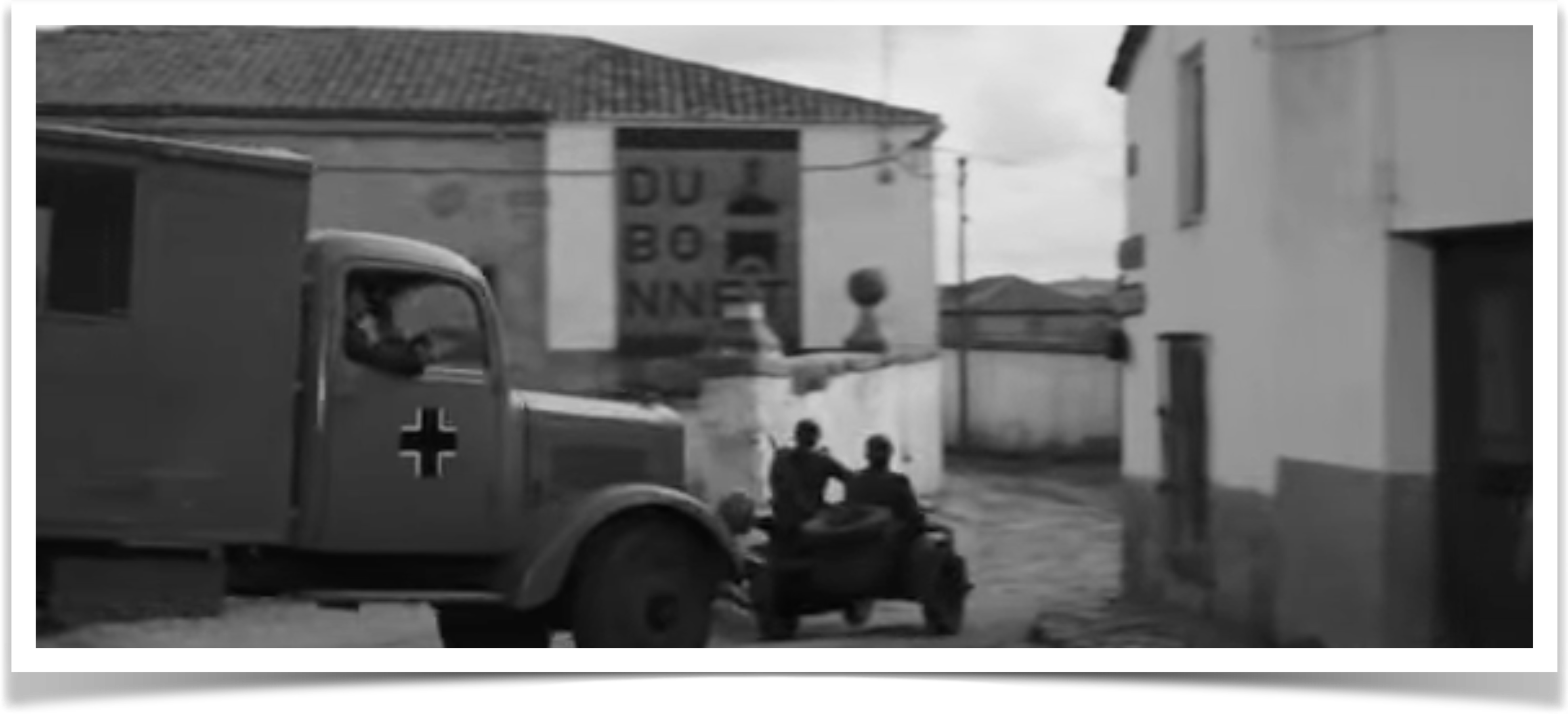 Fotograma de La Brigada de los Condenados con camión militar alemán y soldados en motocicleta saliendo de la plaza de Villamanta