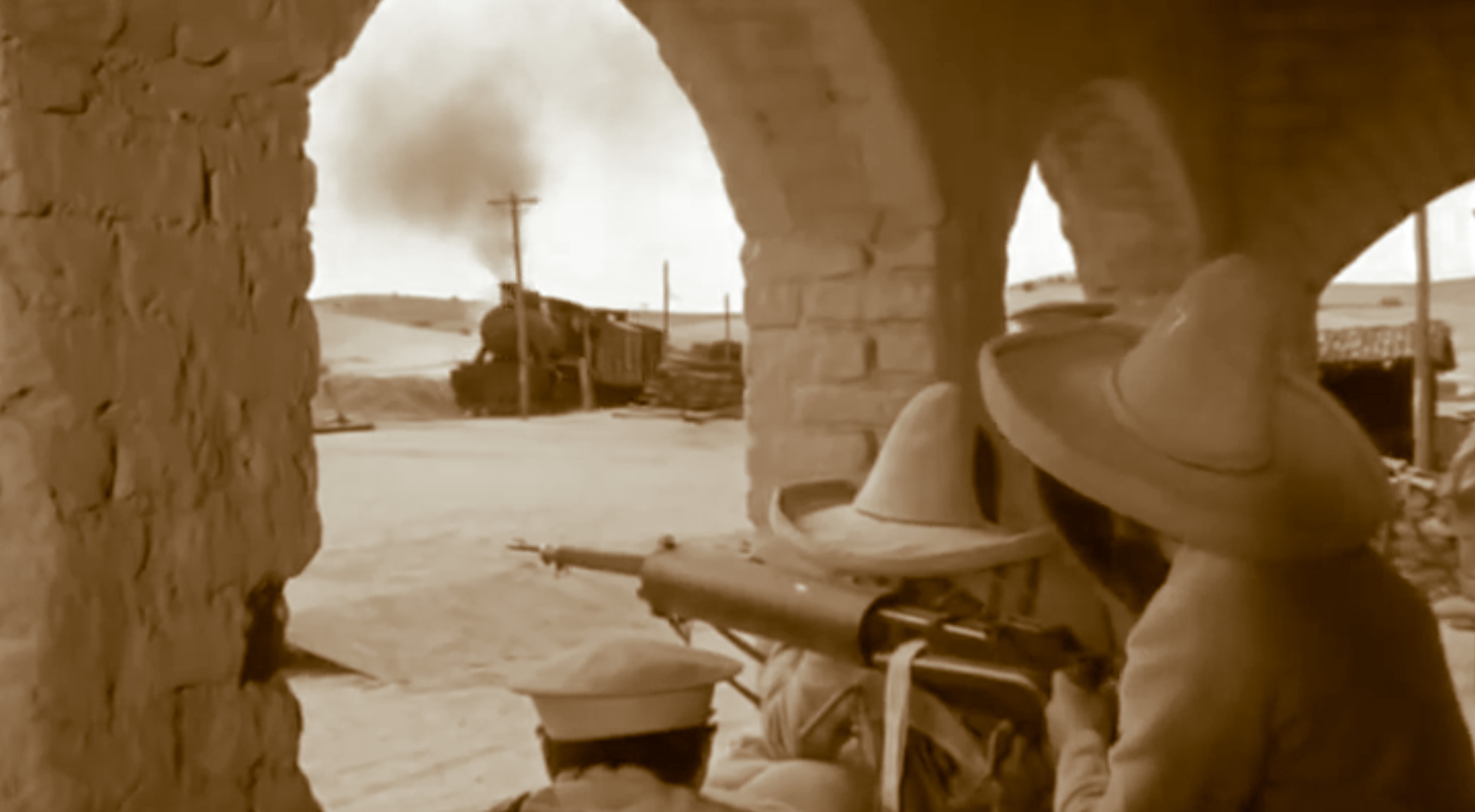 Escena de la película Cien Rifles con guerrilleros yaquis apuntando sus rifles desde un pórtico de piedra mientras un tren militar se aproxima a la estación de Villamanta
