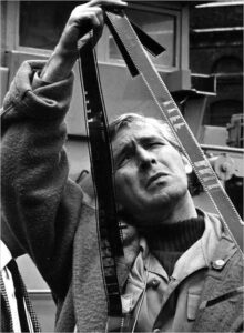 El director Paul Wendkos observa cuidadosamente un rollo de película durante un rodaje, imagen en blanco y negro.